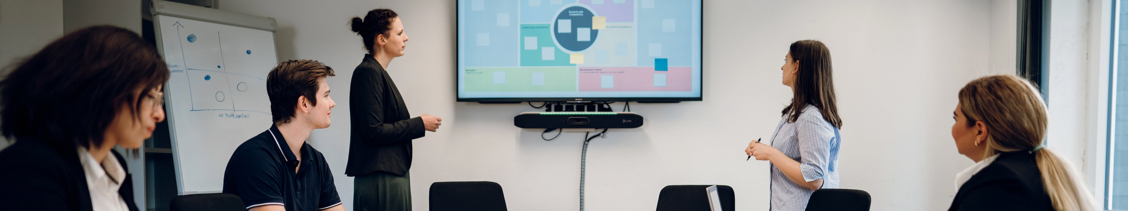 Studierende diskutieren in einem Seminarraum. Im Hintergrund ist eine Präsentation zu sehen. 