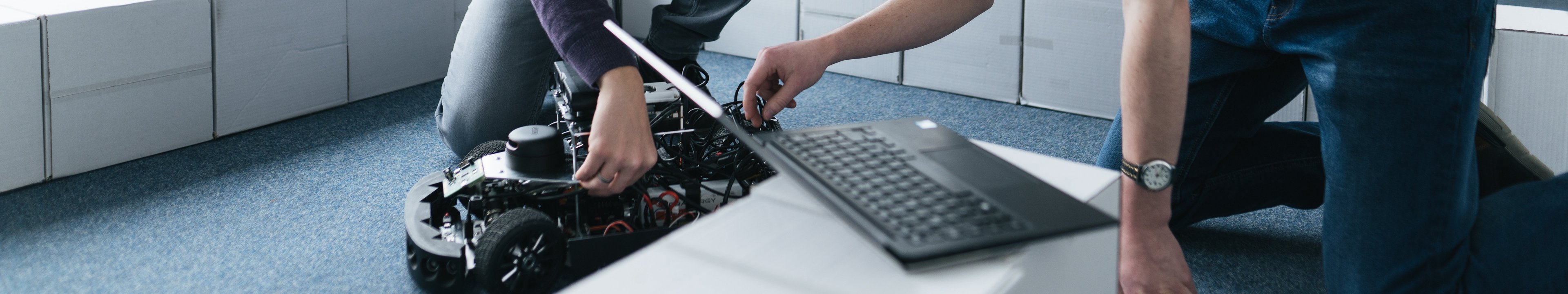 Zwei Personen arbeiten an einem Laptop und einem selbstfahrenden Modellauto